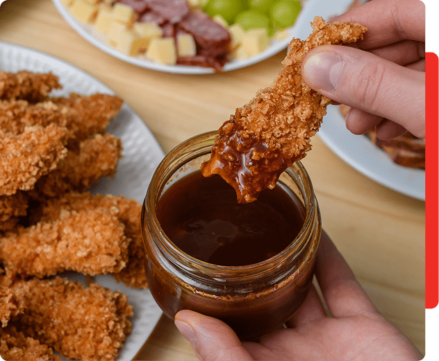 Dipping chicken strip in barbecue sauce jar.
