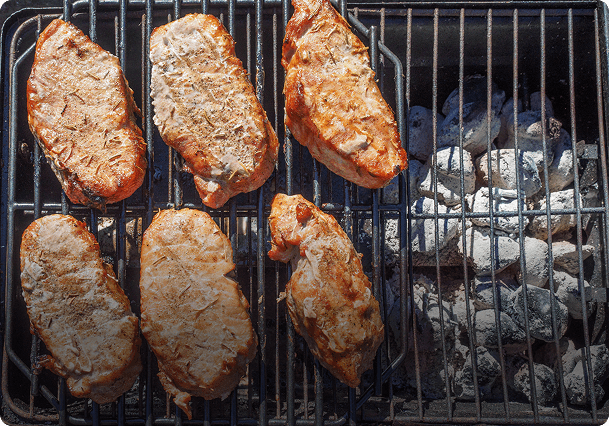 Grilled steaks cooking over charcoal fire.