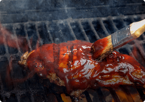 Brushing barbecue sauce on grilled meat.
