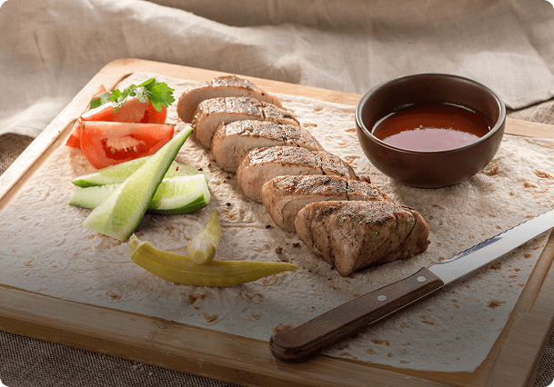 Sliced meat with vegetables and sauce on board.